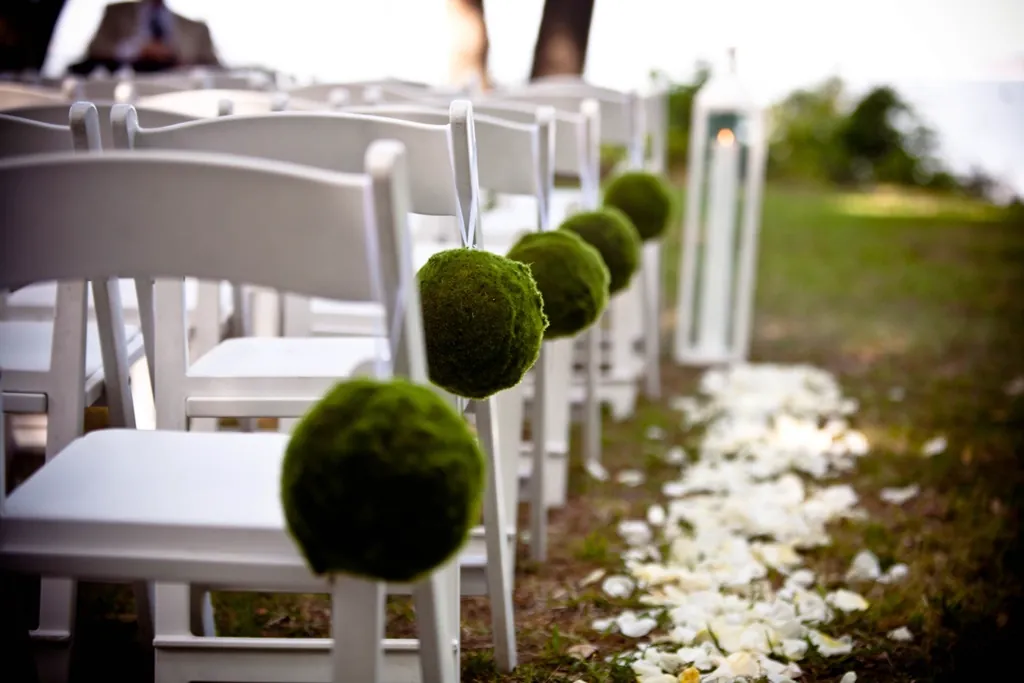 White ceremony chairs with moss balls and petals