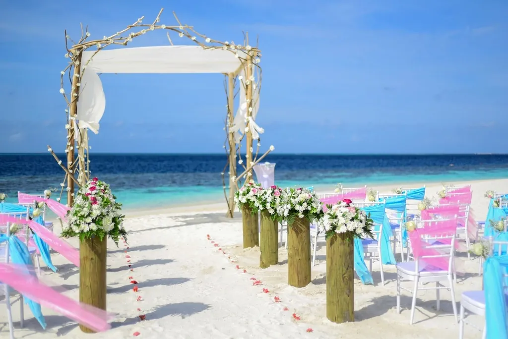 Beach wedding arch with white drapes and pink aisle chairs